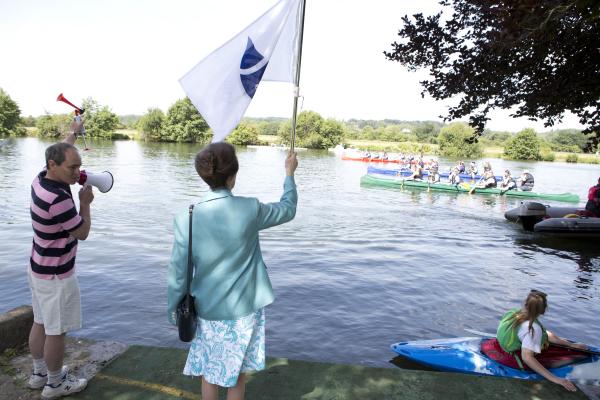 Her Royal Highness the Princess Royal holds a flag by the river to open the Regatta.
